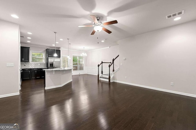 unfurnished living room featuring ceiling fan with notable chandelier and dark hardwood / wood-style flooring