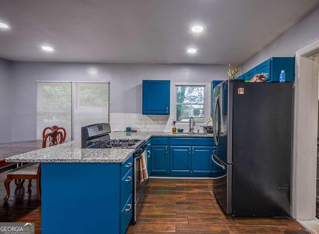 kitchen featuring blue cabinetry, dark hardwood / wood-style floors, gas stove, and refrigerator