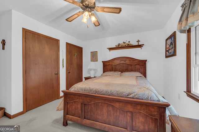 bedroom with light colored carpet, ceiling fan, and two closets