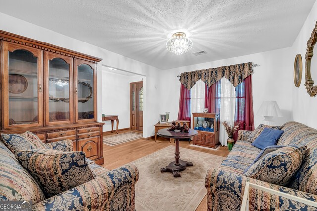 living room with a textured ceiling, a notable chandelier, and light hardwood / wood-style flooring