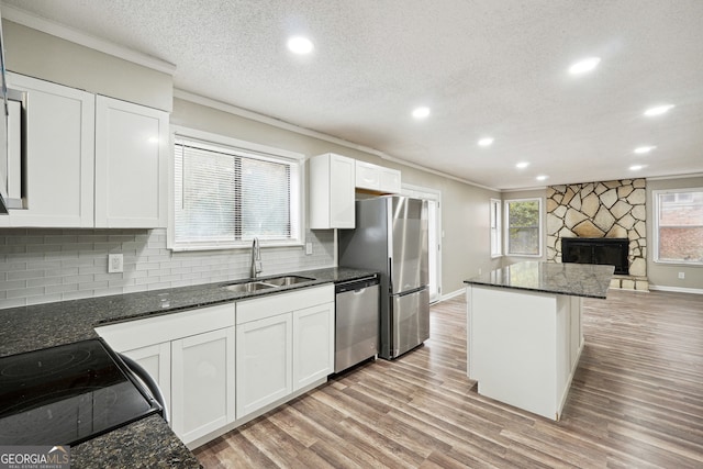 kitchen with light wood-type flooring, appliances with stainless steel finishes, sink, white cabinets, and dark stone countertops