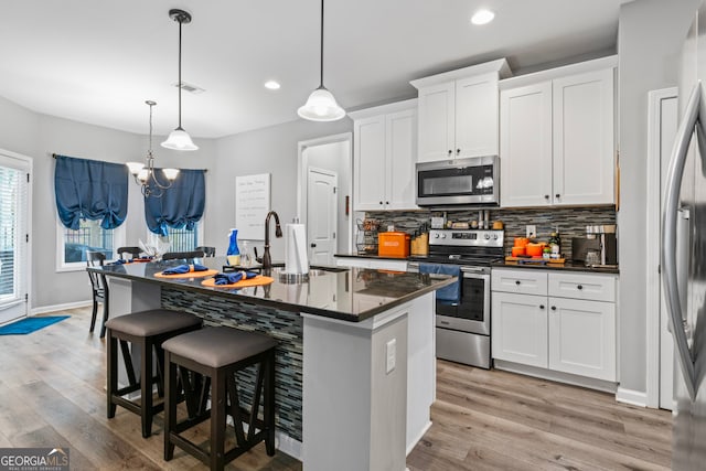 kitchen featuring a center island with sink, white cabinetry, appliances with stainless steel finishes, decorative light fixtures, and light wood-type flooring