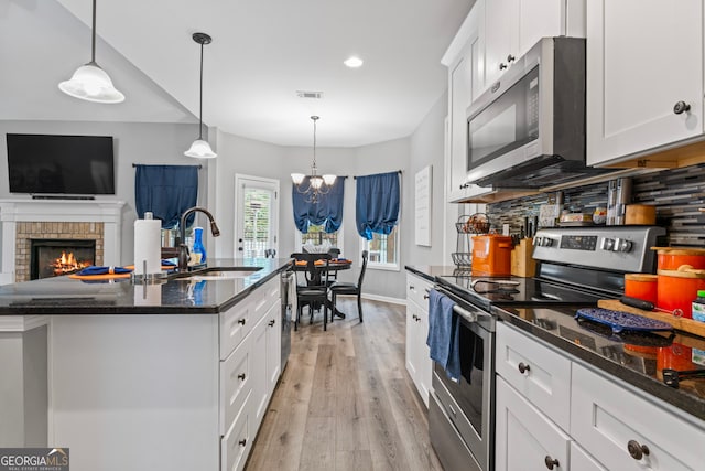 kitchen with stainless steel appliances, sink, decorative light fixtures, an island with sink, and light wood-type flooring