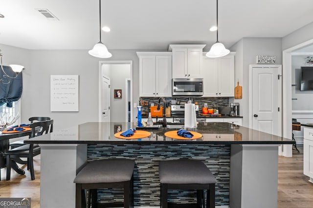 kitchen with stainless steel appliances, light wood-type flooring, pendant lighting, white cabinets, and a center island