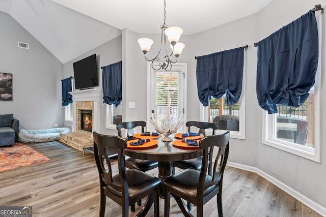 dining space with hardwood / wood-style floors, a fireplace, lofted ceiling, and a chandelier