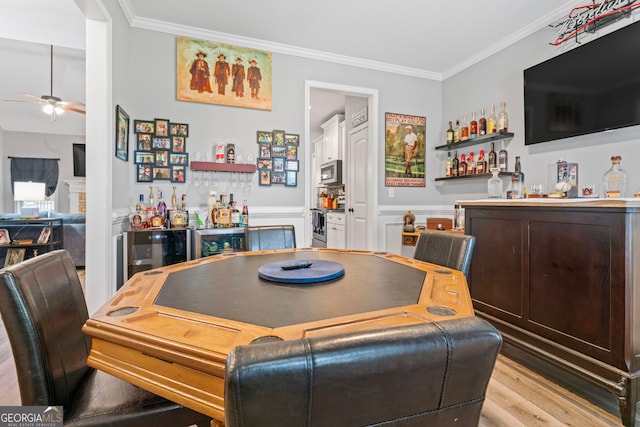 bar with stainless steel appliances, light hardwood / wood-style floors, ceiling fan, and crown molding