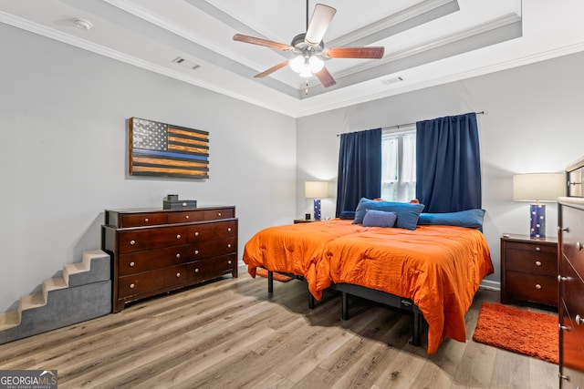 bedroom with ceiling fan, a tray ceiling, light hardwood / wood-style flooring, and ornamental molding