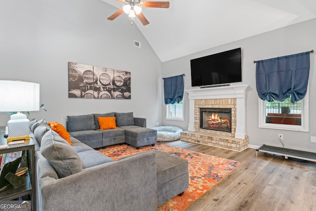 living room with a brick fireplace, ceiling fan, light hardwood / wood-style flooring, and high vaulted ceiling