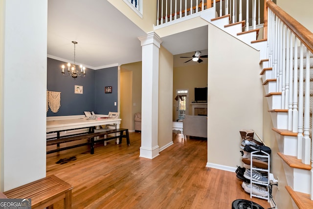 foyer with wood-type flooring, crown molding, a high ceiling, decorative columns, and ceiling fan with notable chandelier