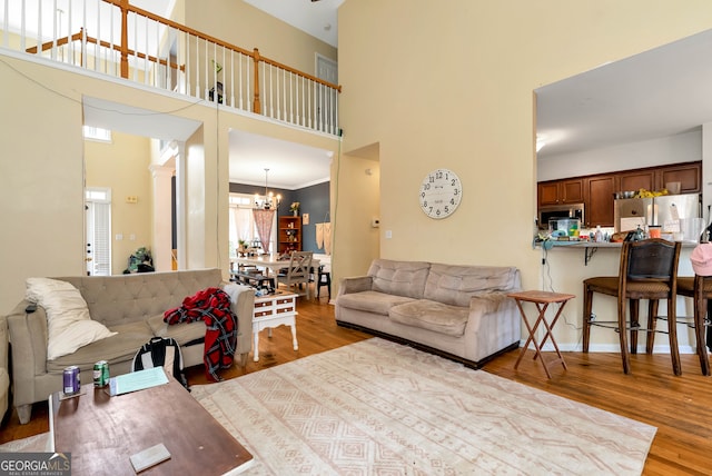 living room featuring crown molding, light hardwood / wood-style flooring, a chandelier, and a high ceiling