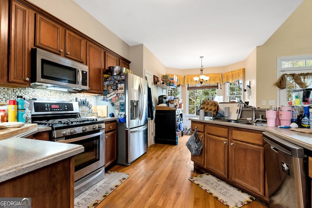 kitchen featuring light hardwood / wood-style floors, stainless steel appliances, a notable chandelier, sink, and decorative light fixtures