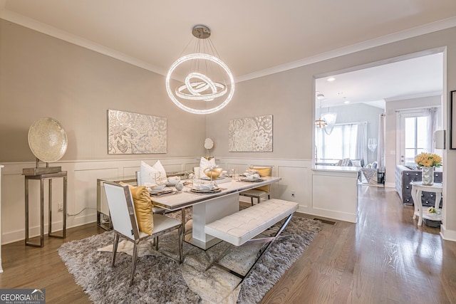 dining space with hardwood / wood-style flooring, ornamental molding, and a notable chandelier