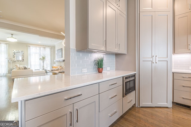 kitchen featuring light stone counters, light wood-type flooring, kitchen peninsula, and backsplash