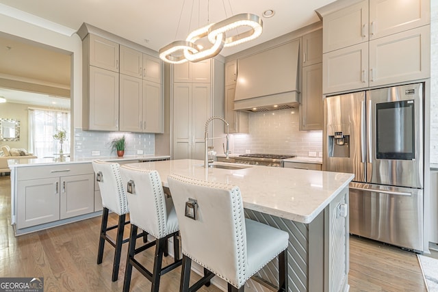 kitchen featuring tasteful backsplash, stainless steel fridge, hanging light fixtures, sink, and light hardwood / wood-style floors