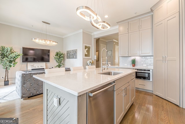 kitchen with stainless steel appliances, sink, hanging light fixtures, a kitchen island with sink, and light wood-type flooring