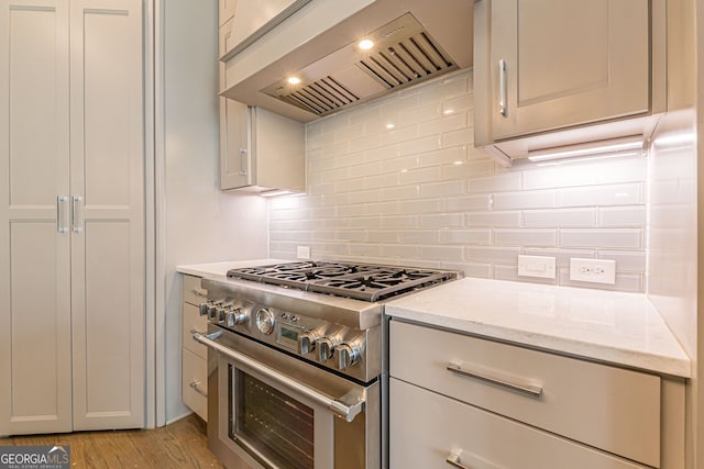 kitchen featuring light stone countertops, custom exhaust hood, light hardwood / wood-style flooring, high end stainless steel range oven, and decorative backsplash