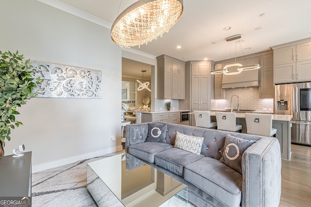 living room with light hardwood / wood-style floors, sink, a notable chandelier, and ornamental molding