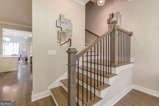 staircase featuring wood-type flooring, a notable chandelier, and crown molding