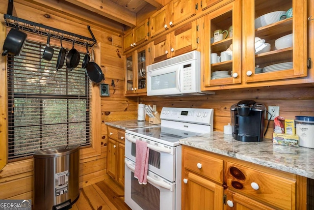 kitchen featuring hardwood / wood-style floors, light stone counters, wood walls, and white appliances