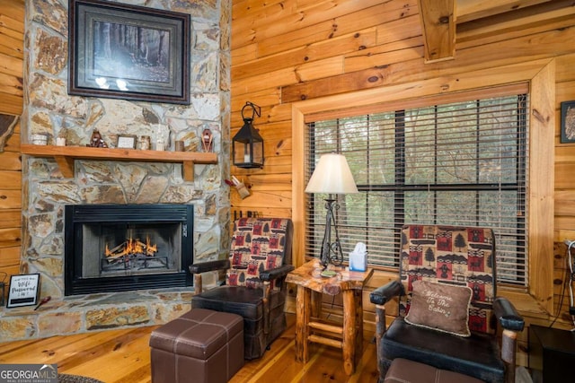 sitting room with beamed ceiling, wooden walls, a stone fireplace, and wood-type flooring