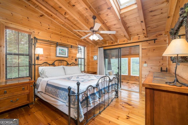 bedroom with lofted ceiling with skylight, wooden walls, hardwood / wood-style flooring, and ceiling fan