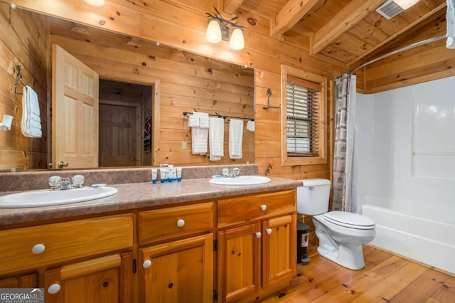 full bathroom featuring beamed ceiling, wood-type flooring, vanity, wooden walls, and toilet