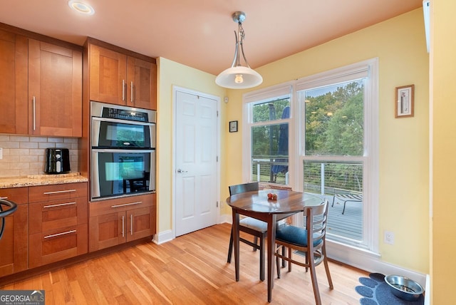 kitchen with light stone counters, backsplash, hanging light fixtures, stainless steel double oven, and light wood-type flooring