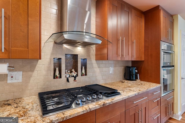 kitchen featuring stainless steel appliances, light stone counters, tasteful backsplash, exhaust hood, and light wood-type flooring