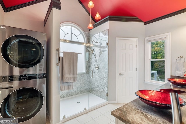 bathroom featuring stacked washing maching and dryer, tile patterned flooring, a healthy amount of sunlight, and a shower with shower door