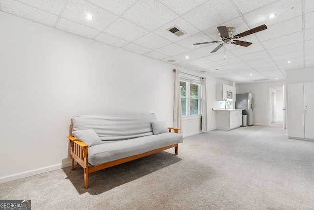 sitting room with a drop ceiling, light carpet, and ceiling fan