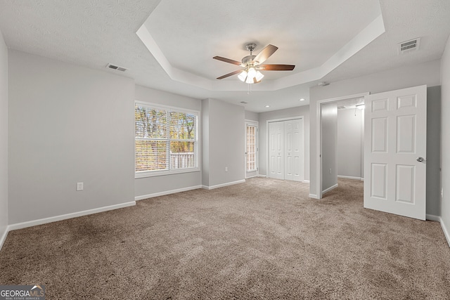 unfurnished bedroom featuring carpet flooring, a textured ceiling, a raised ceiling, ceiling fan, and a closet