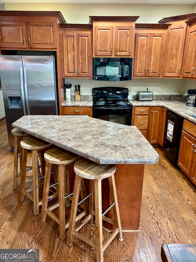 kitchen with a breakfast bar, black appliances, and light hardwood / wood-style flooring