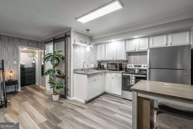 kitchen with white cabinets, appliances with stainless steel finishes, a barn door, and decorative light fixtures