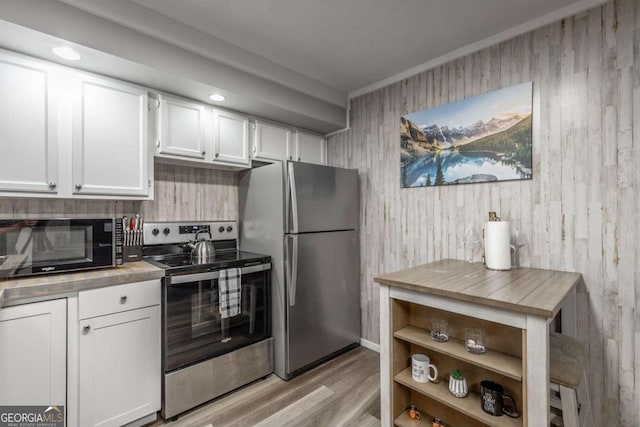 kitchen featuring white cabinets, wooden walls, light hardwood / wood-style flooring, and stainless steel appliances