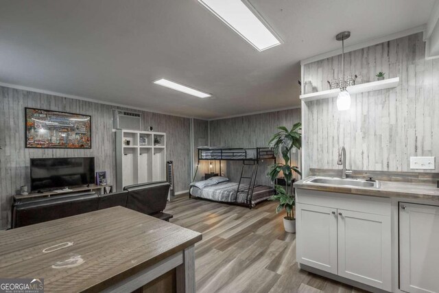 bedroom featuring wood walls, sink, a wall mounted AC, crown molding, and light wood-type flooring