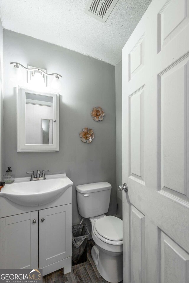 bathroom featuring a textured ceiling, vanity, hardwood / wood-style flooring, and toilet