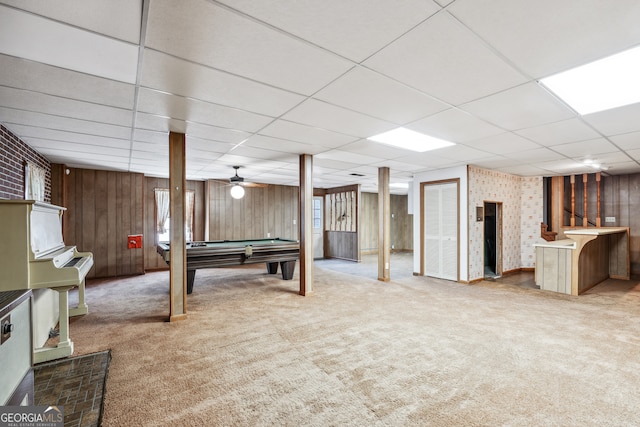 rec room with light carpet, a drop ceiling, ceiling fan, wooden walls, and billiards