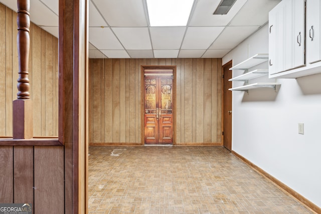 unfurnished room with a paneled ceiling and wooden walls