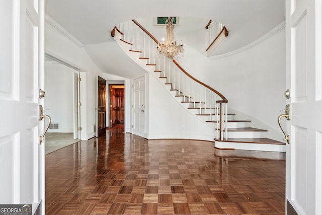 foyer entrance with a chandelier, dark parquet flooring, and ornamental molding