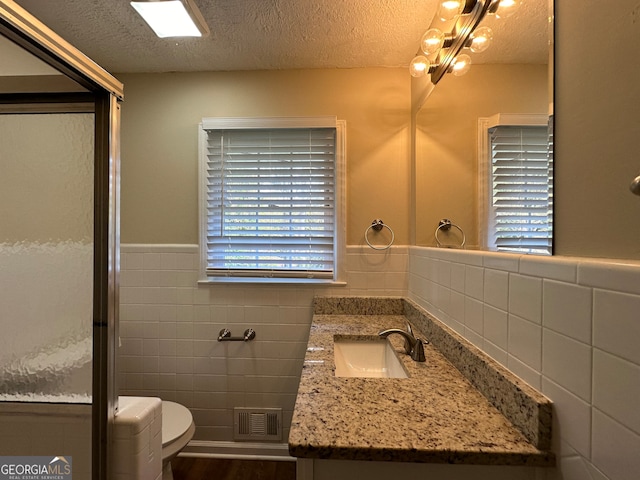 bathroom with vanity, toilet, a textured ceiling, and tile walls