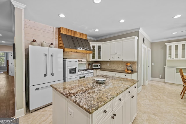 kitchen featuring ventilation hood, white cabinetry, light stone countertops, white appliances, and a center island