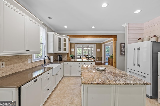 kitchen with a healthy amount of sunlight, refrigerator, white cabinets, sink, and a kitchen island