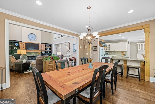 dining space with a stone fireplace, a notable chandelier, hardwood / wood-style flooring, and crown molding