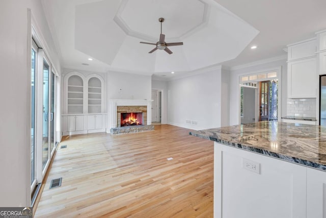 kitchen with dark stone countertops, a stone fireplace, light hardwood / wood-style flooring, white cabinets, and decorative backsplash