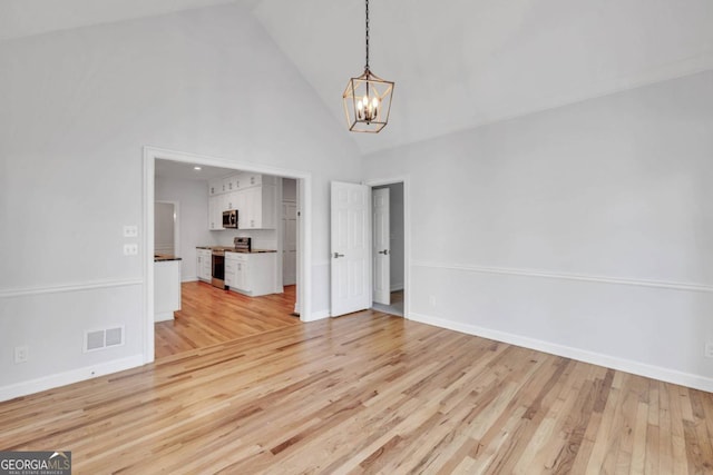 unfurnished living room with high vaulted ceiling, a chandelier, and light hardwood / wood-style floors