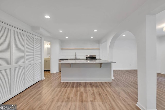 kitchen featuring sink, stainless steel range, a kitchen island, a breakfast bar, and light hardwood / wood-style flooring