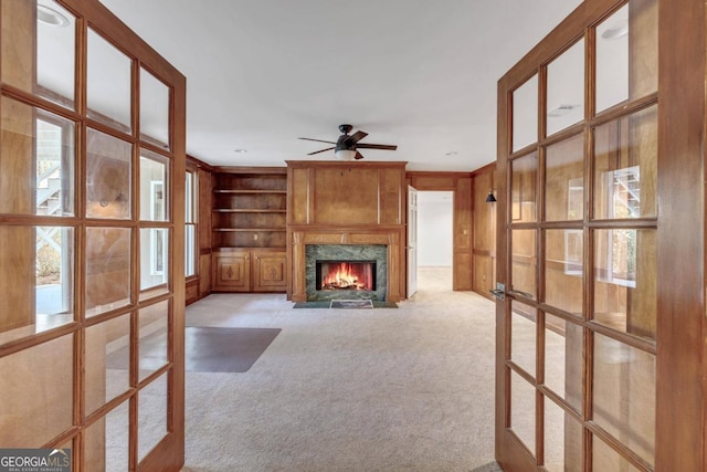 unfurnished living room with ceiling fan, light colored carpet, built in features, and a high end fireplace