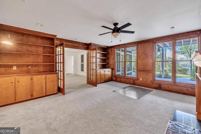 unfurnished living room featuring french doors, wooden walls, light carpet, and ceiling fan