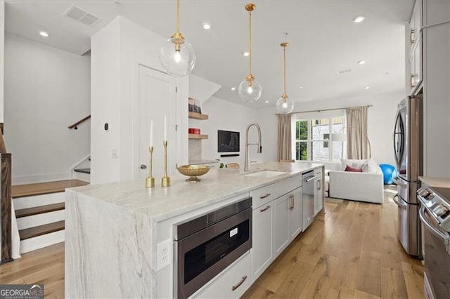 kitchen with white cabinetry, light hardwood / wood-style floors, a center island with sink, and decorative light fixtures