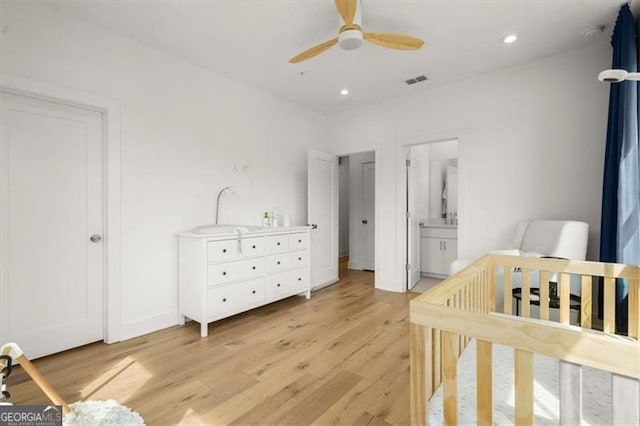 bedroom with a crib, ceiling fan, connected bathroom, and light hardwood / wood-style flooring